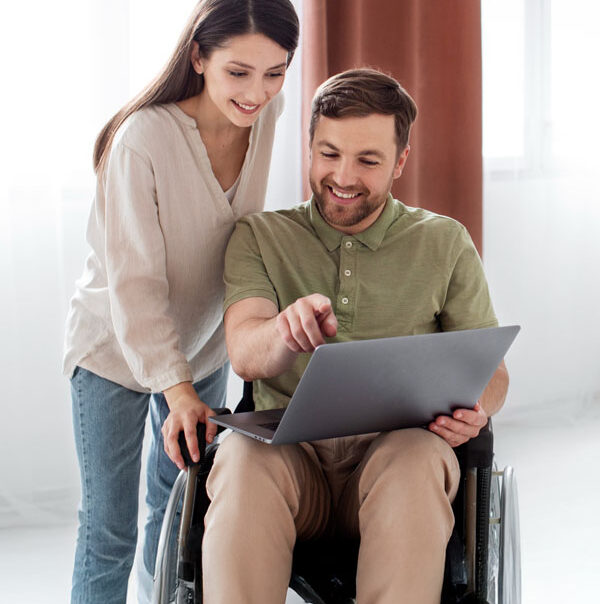 Aus Care Community Services | Local NDIS Providers | What Does an NDIS Support Worker Do at Home? Support worker helping a person who uses a wheelchair with a laptop at home