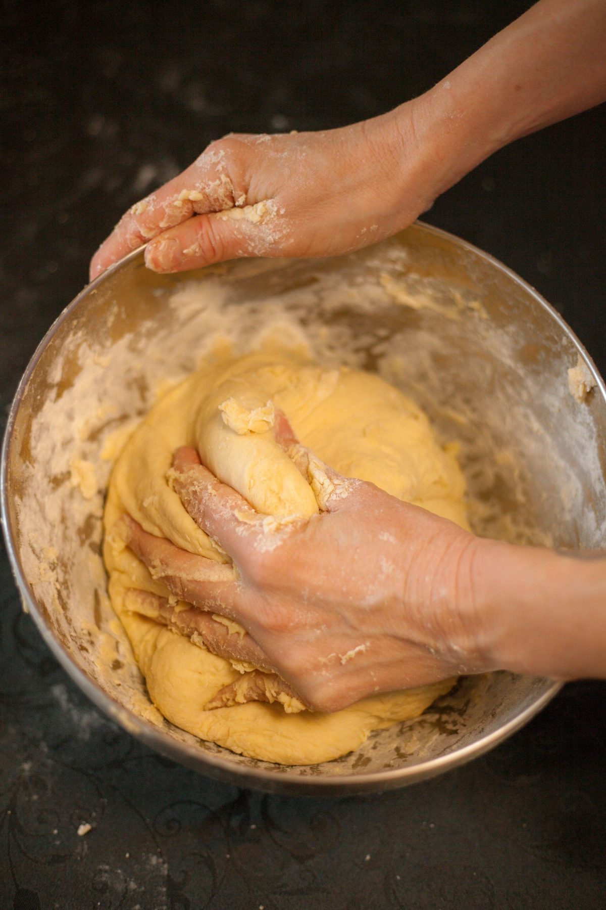 Hands kneading dough in a mixing bowl on a kitchen bench