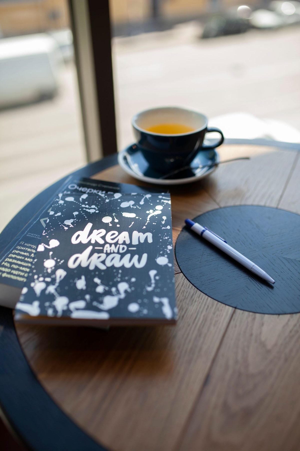 A notebook, pen and cup of tea on a wooden table by a window